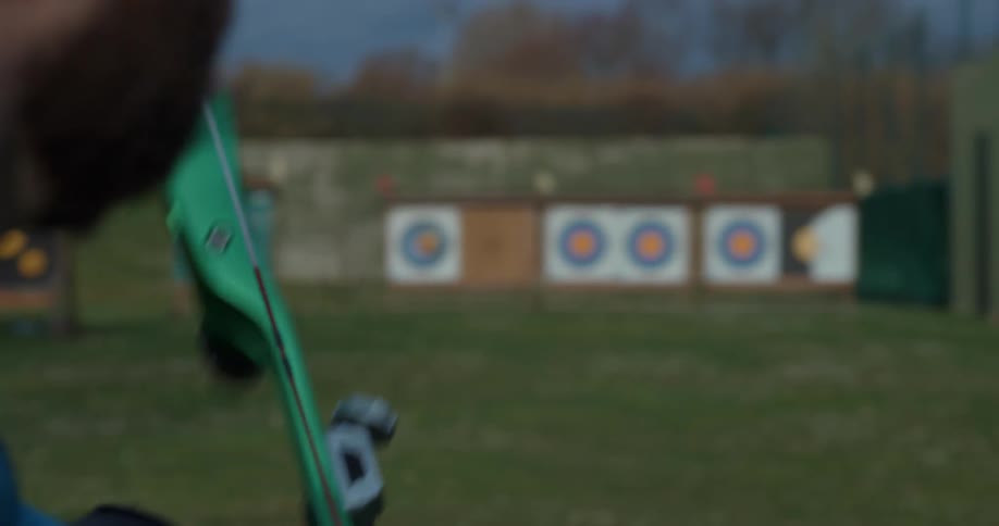 A person uses a bow to shoot arrows at a circular target on a field