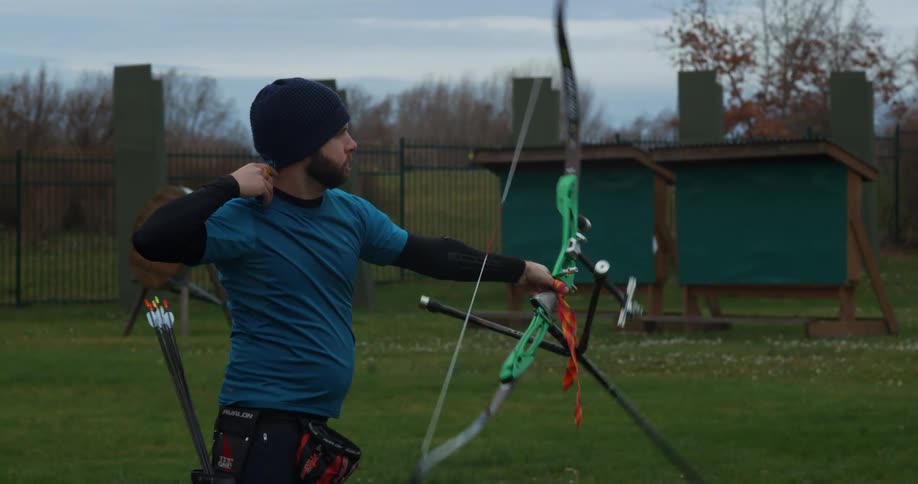 A man in a field shoots an arrow with a bow