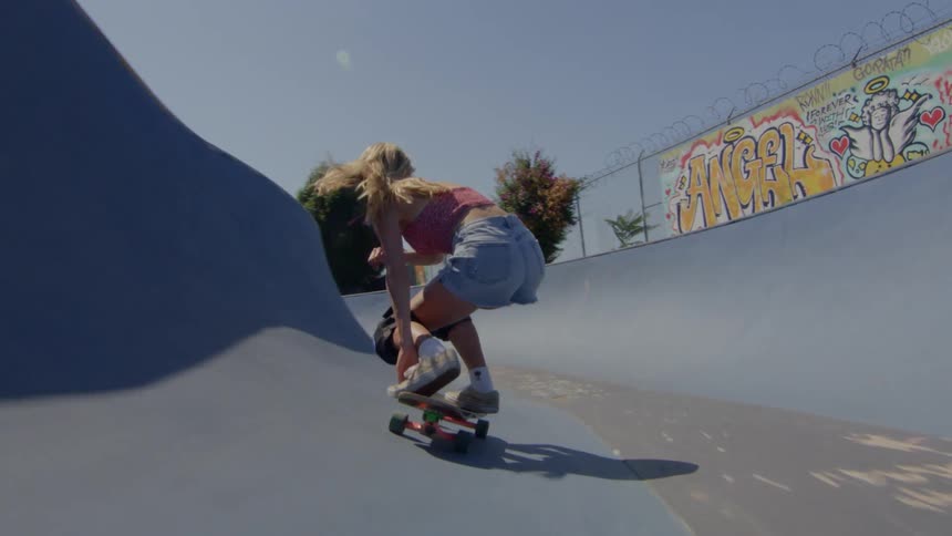 A teen girl wearing denim shorts is riding a skateboard at the skatepark on a sunny day