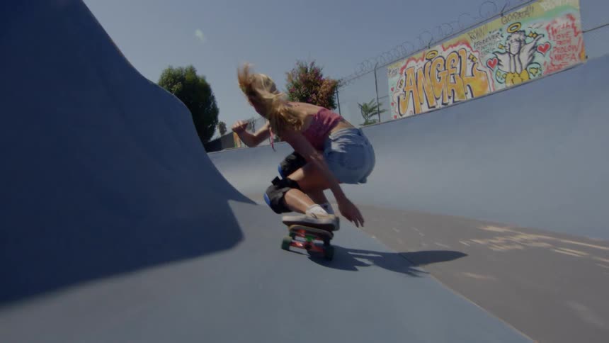 A woman shown from behind rides a skateboard down a long ramp