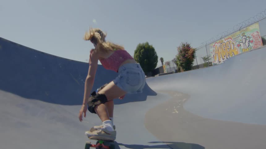 A blonde woman is riding a skateboard and pushing off with her feet