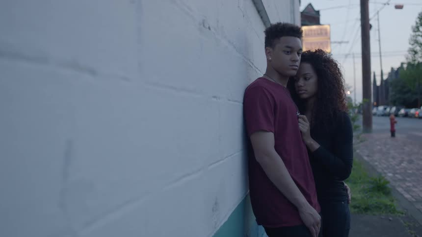 A woman is leaning against a man by a wall