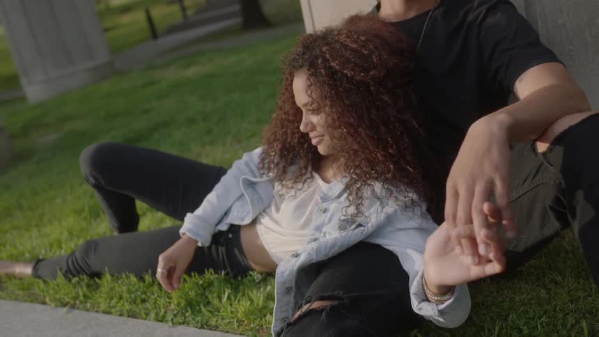 A man and woman are sitting on the grass by a sidewalk