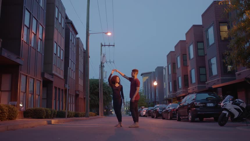 A man and woman dance on an empty street at sunset
