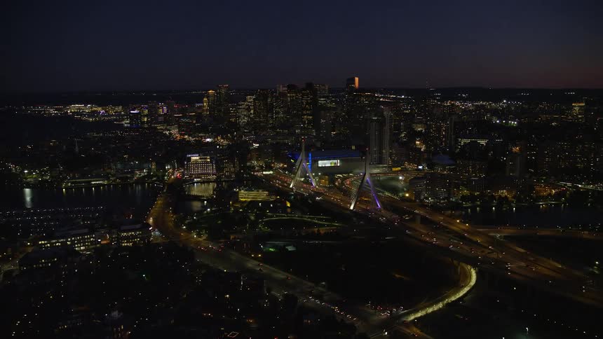 Traffic moving through city scape at night passes over bridge with angular arches near downtown