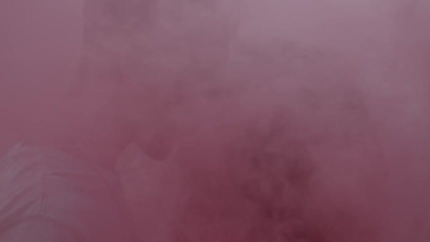 Two people kiss while pink smoke surrounds them
