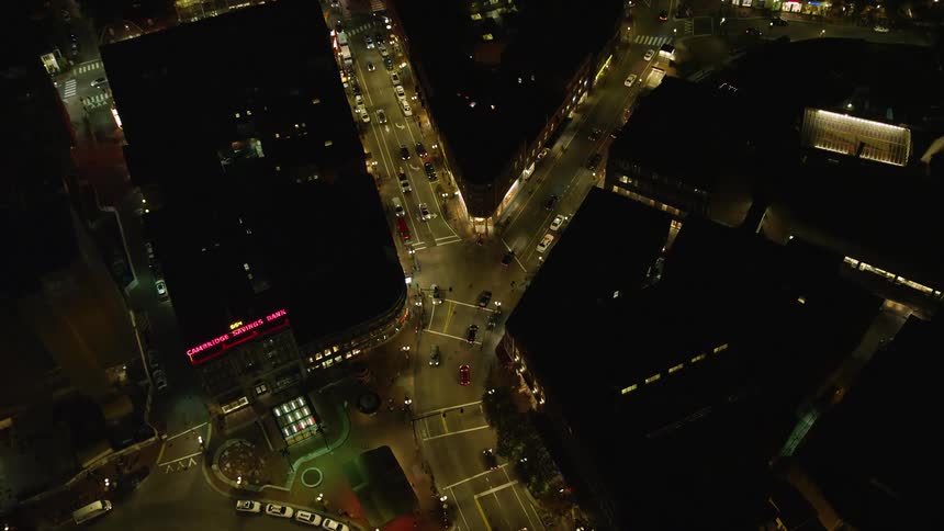 An intersection of streets with many cars passing by in a city at night with streetlights