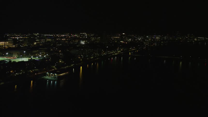 Traffic flows along streets near water reflecting waterfront lights at night