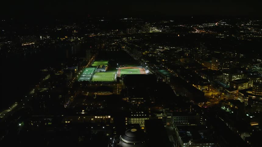 Night flight over a well lit stadium in a city