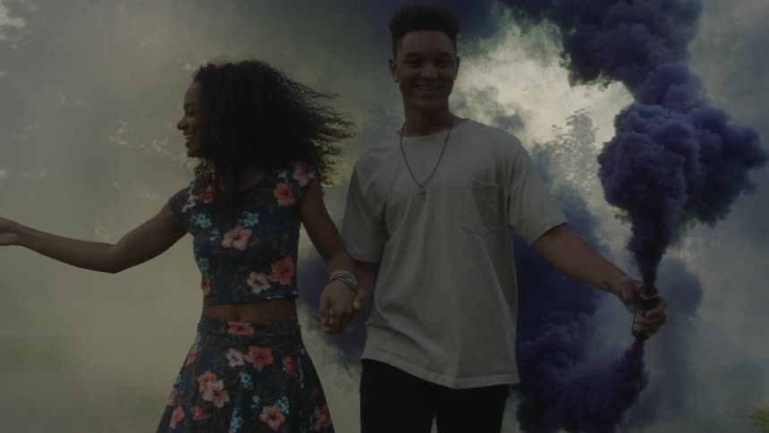 Two people walk holding smoke cans pouring out blue and yellow smoke