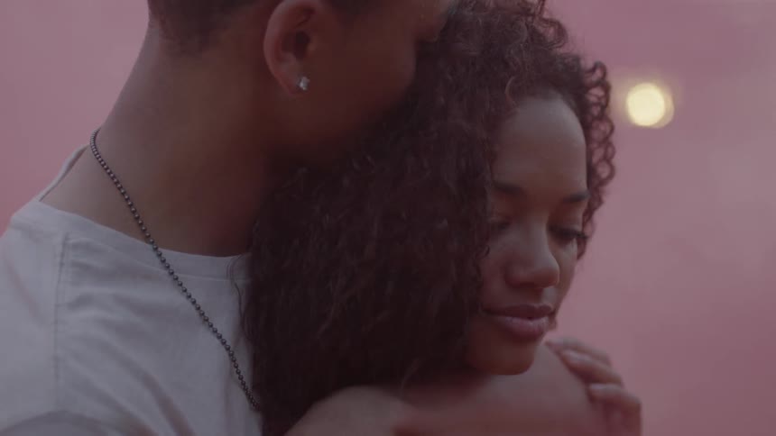 A man hugs a woman from behind with pink smoke all around