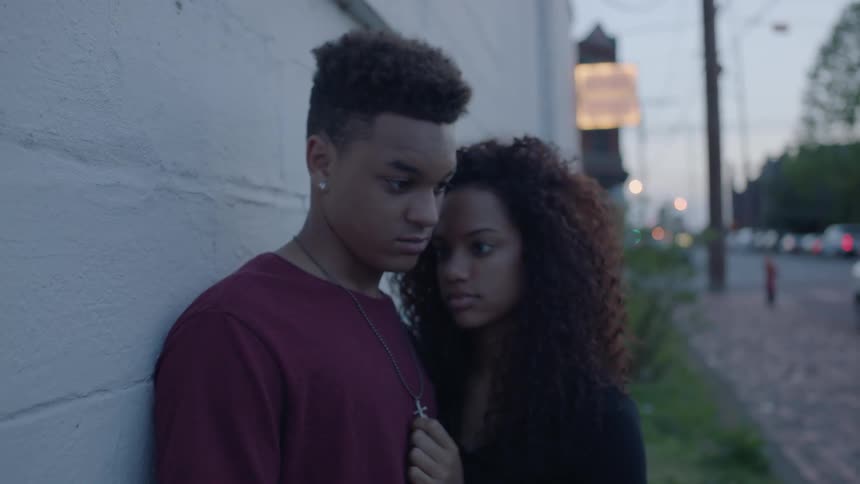 A woman is touching a man's chest who is leaning against a wall