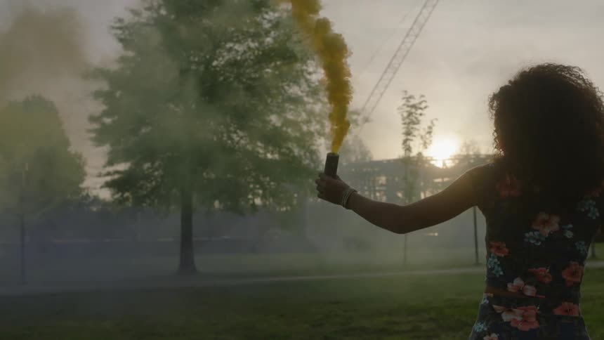 A woman walks tracing yellow smoke in the air