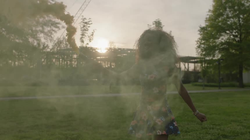 A woman is walking with a smoke can in her hand giving off smoke everywhere