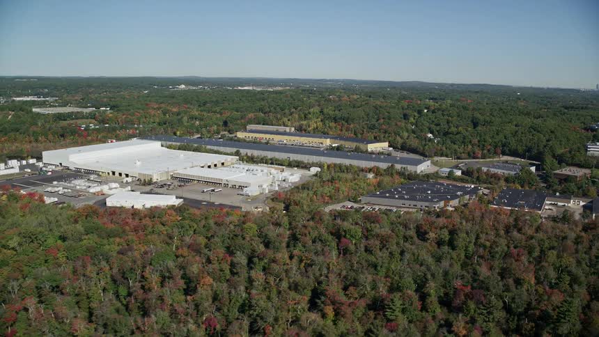 Trees in woods surrounding commercial buildings with parking lots change colors during fall