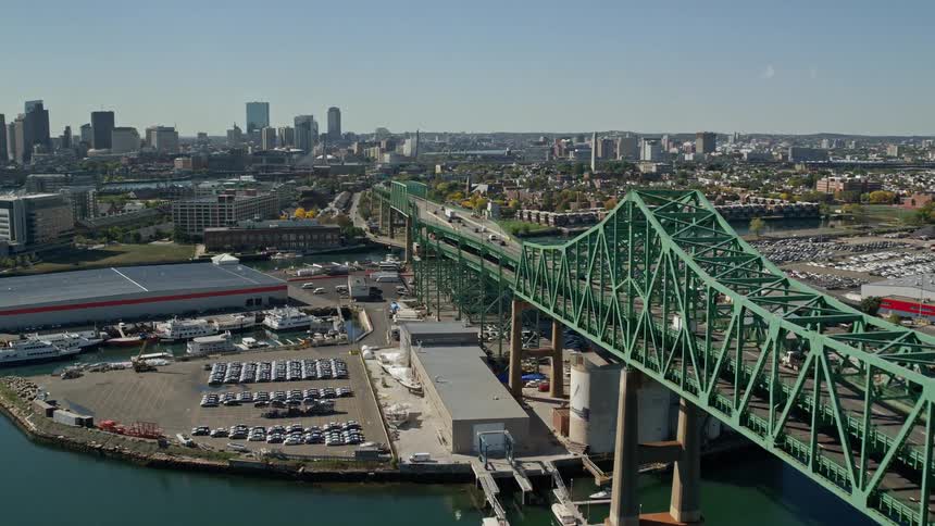 A bridge with a green iron frame that passes over the sea and right behind it is the metropolitan part of a city