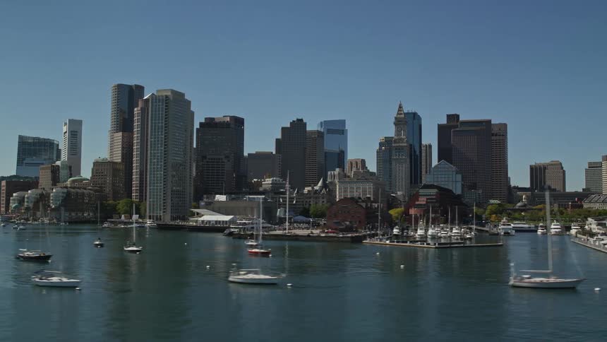 A metropolitan city with huge buildings and on the seafront with several boats in the water