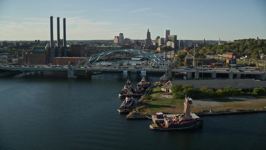 A city with a bridge that passes over the sea and has many cars passing by and behind large buildings