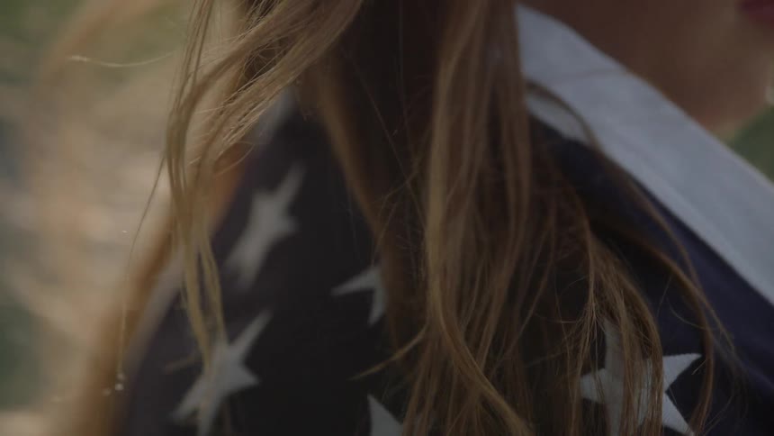 A woman's hair blows over a flag around her shoulders