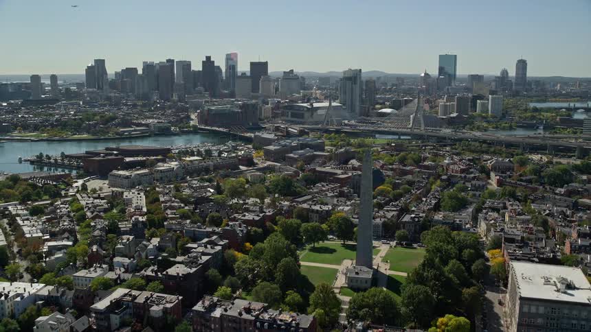 A daytime aerial view of a city on the waterfront with a large bridge and monument