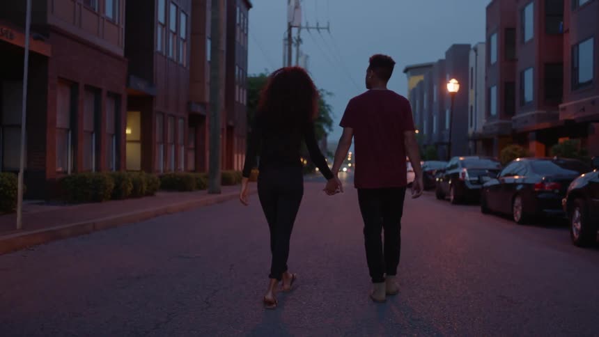 A man and woman hold hands walking down a street