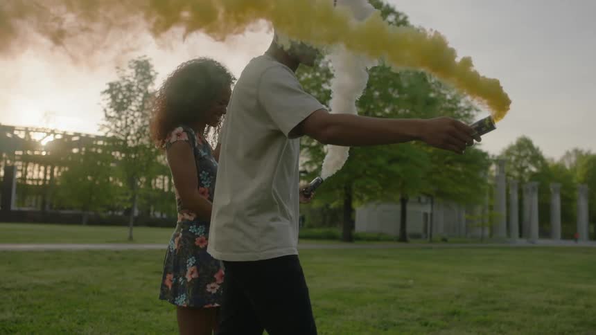 Two people are holding hands on the grass waving smoke cans around