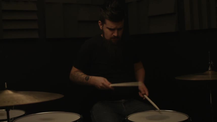 A man is playing drums in a dark studio