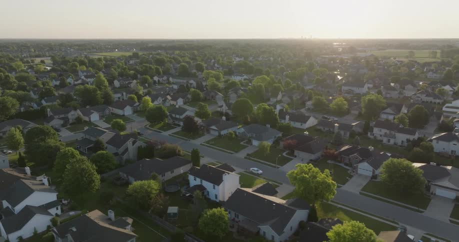 Gentle orbit over a nice suburban neighborhood as the sun hangs low on the horizon