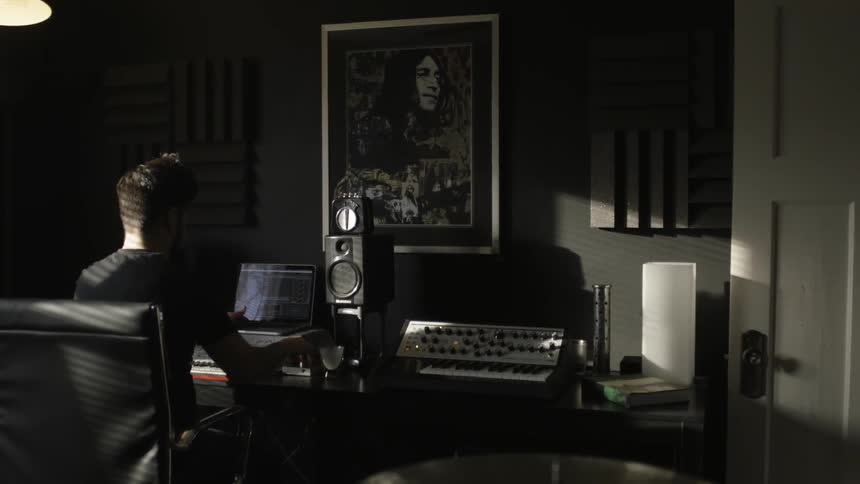 A man is sitting at some musical equipment in a dark room