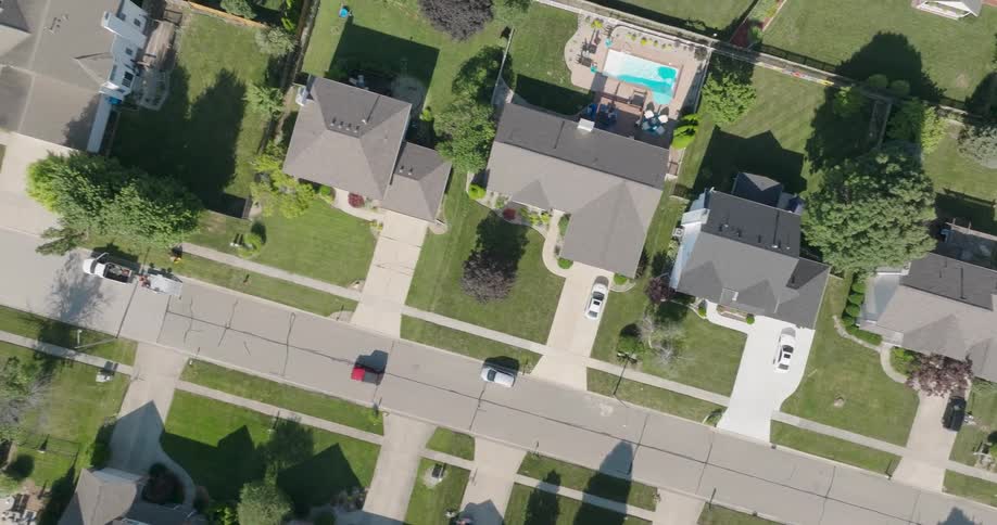 Birds eye view of a red car driving through a peaceful suburban neighborhood