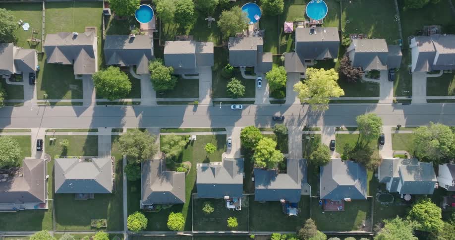 Lush green yards and round blue swimming pools dot the yards of a nice suburban neighborhood
