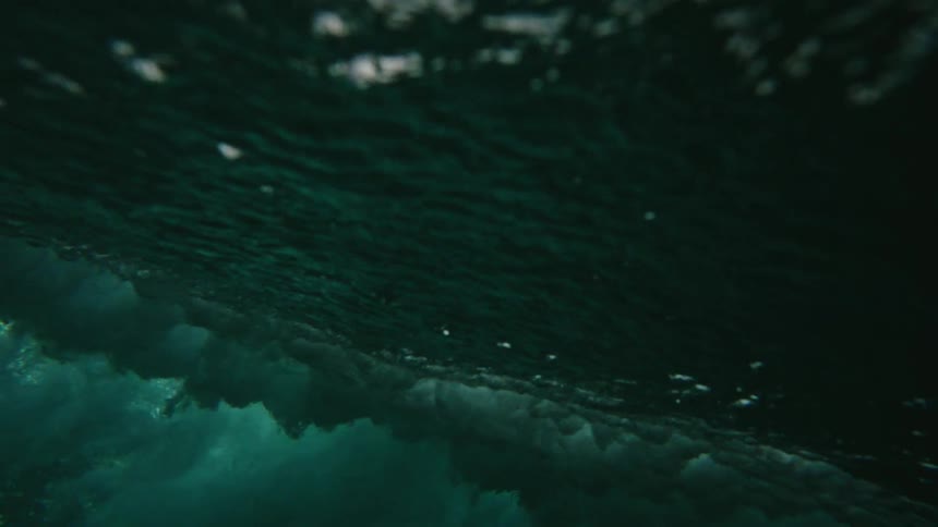 Rough water waves splash as they roll in under a dark cloudy sky and move across the water