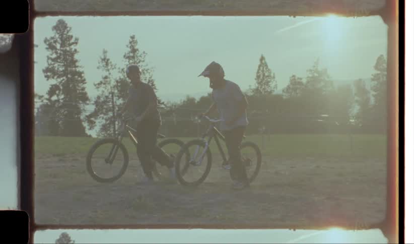 Two men push their bmx bikes on the field