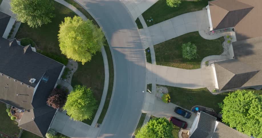Following directly above a curved street between homes in a peaceful neighborhood
