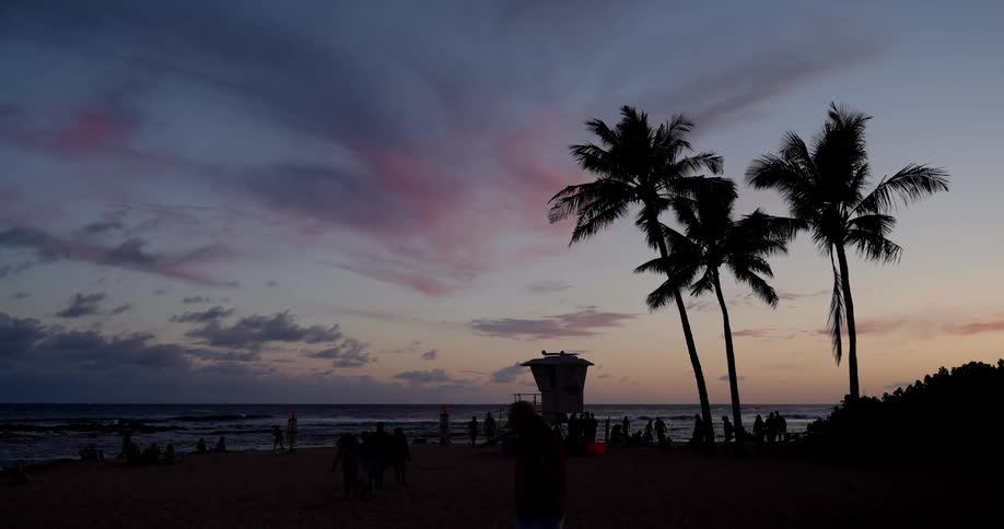 Landscape of a beach with several people under a purple evening sky