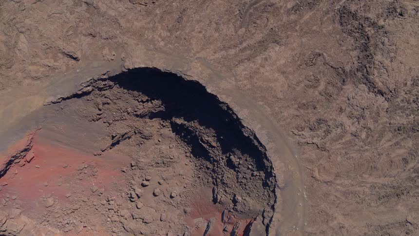 Top down twisting reveal of colorful rock within a deep crater surrounded by solidified lava