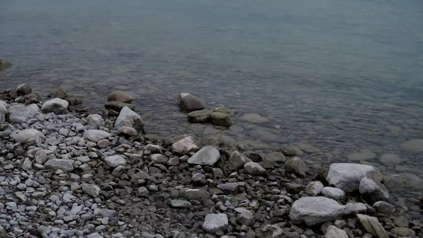 Rocks and pebbles cover the ground as water ripples along the shoreline