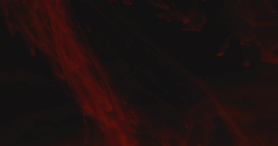 Gauzy orange dye floats through liquid under dim lighting