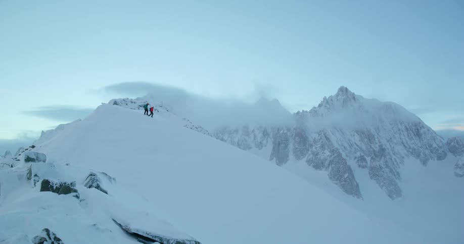 Two hikers descend a snowcovered mountain under blue skies