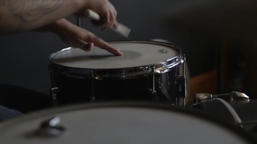 A person is using a drum stick to tap around drums