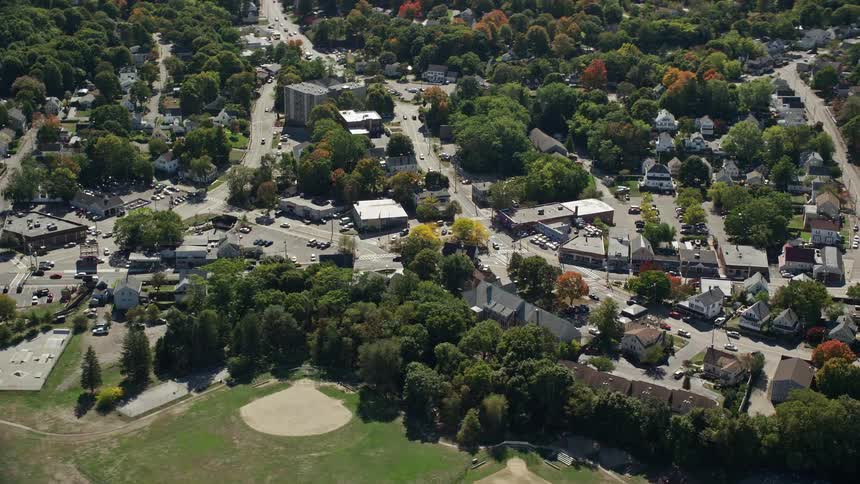 Traffic moves on busy roads near buildings and suburban neighborhoods filled with houses and trees in fall colors around a lake