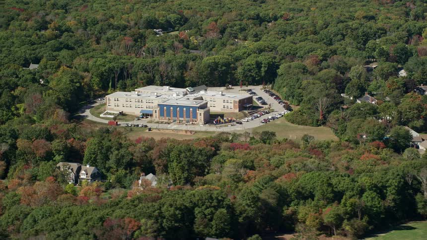 Cars are parked around a school surrounded by fall colored trees and suburban houses