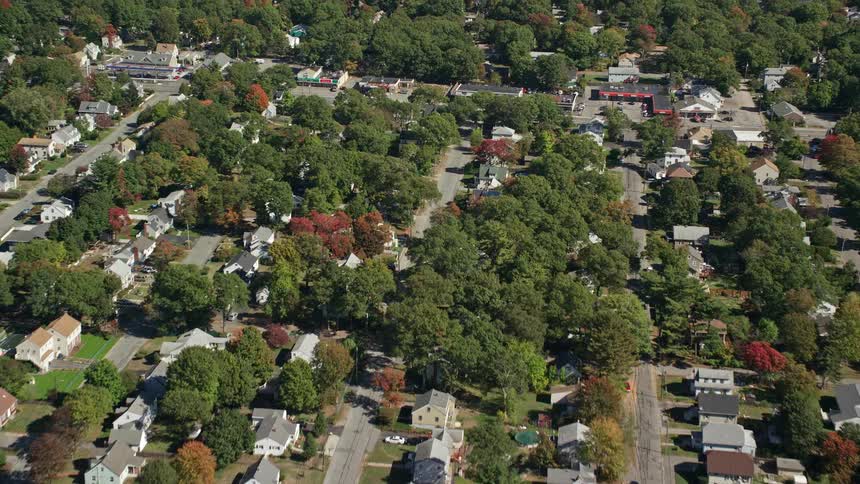 Traffic moves on roads in a suburban neighborhood filled with houses and trees in fall colors near a lake