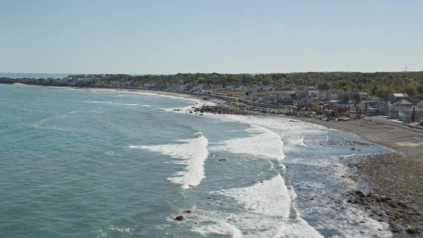 Flight over a rocky beach and a waterfront town by the ocean on a sunny day