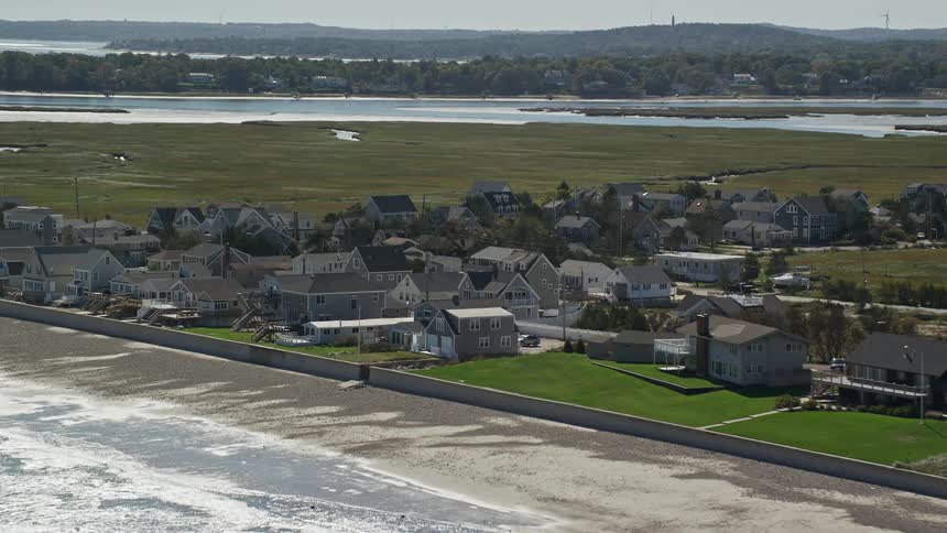 Waves roll in over the beach near a neighborhood of coastal homes as a seagull files over the sand