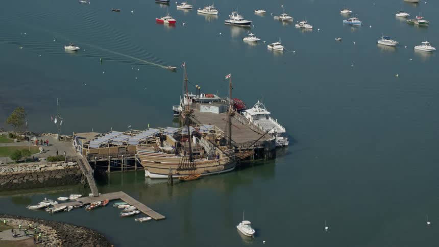 A ferry and masted ship are docked along the pier with small boats sailing in the water