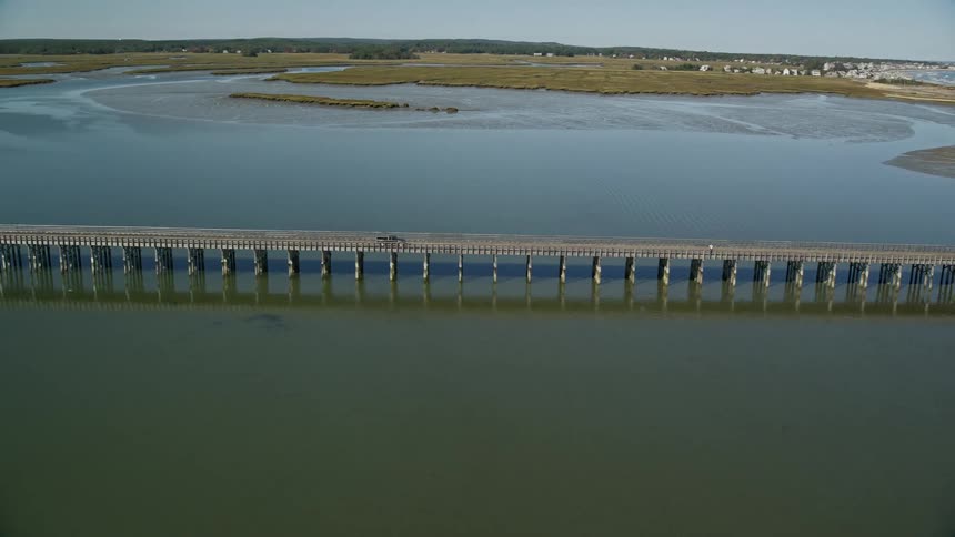 Truck drives along causeway toward beach across lagoon from coastal town