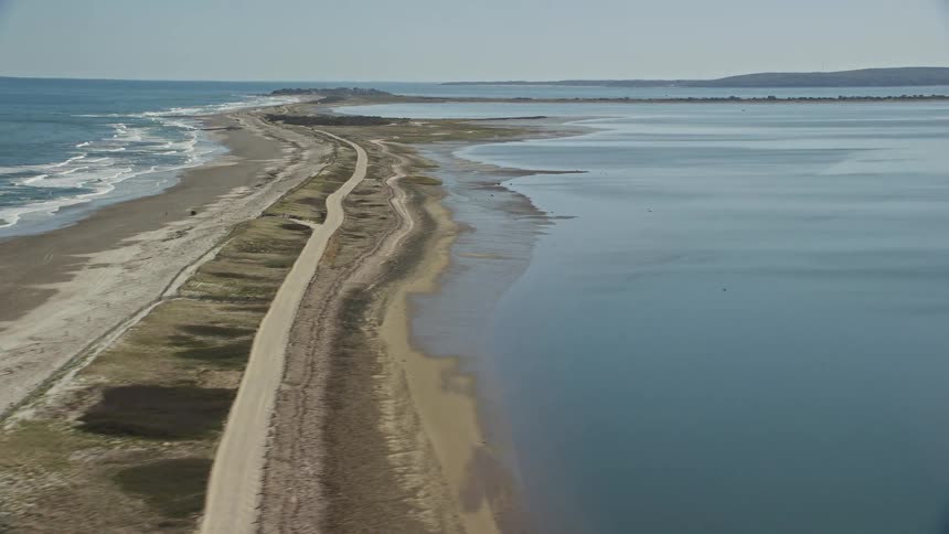 Aerial view from a drone flight over a road on the coast with the ocean on the left and a large lake on the right