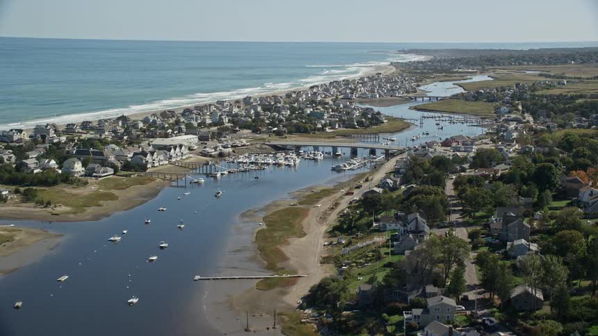 Boats are sailing in a river and parked in a marina alongside a waterfront community on cape cod bay
