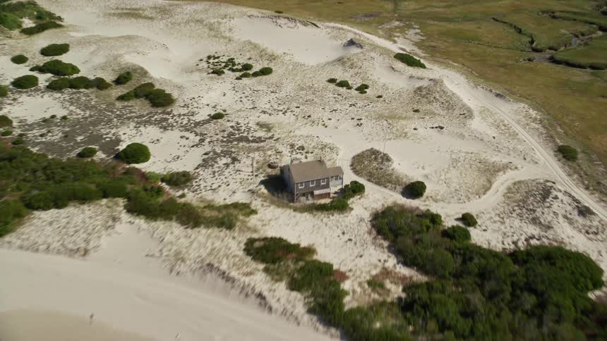 Aerial landscape shot of flat land area next to the coast with a house in the middle of the sand during day time